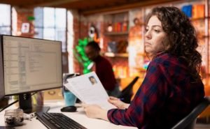 Une recruteuse examine un CV imprimé tout en regardant un autre CV sur son écran d'ordinateur.